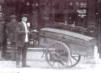 875395 Portret van bakkersknecht Jan de Groot (Hogelanden O.Z. 15) te Utrecht, bij een bakkerskar op een onbekende ...